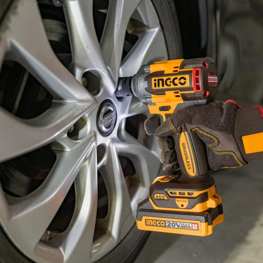 A close-up of a person wearing a black and gray work glove using an iNCC0 cordless impact wrench to tighten a silver car wheel lug on a vehicle tire.